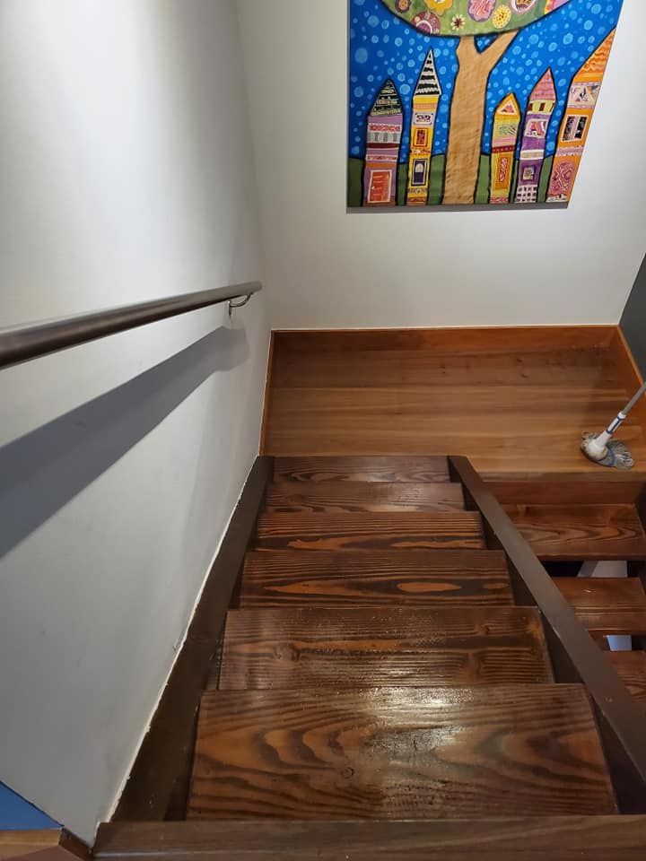 Wooden staircase with handrail, descending from a landing with artwork, white wall, and hardwood floor.