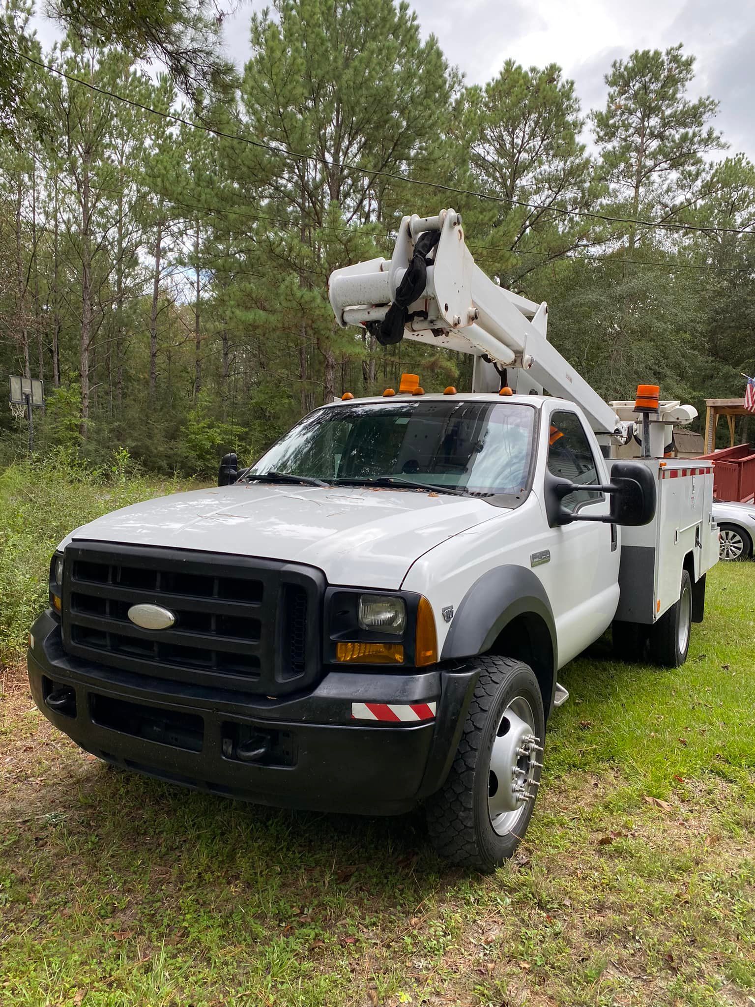 A white truck with a crane on top of it is parked in the grass.
