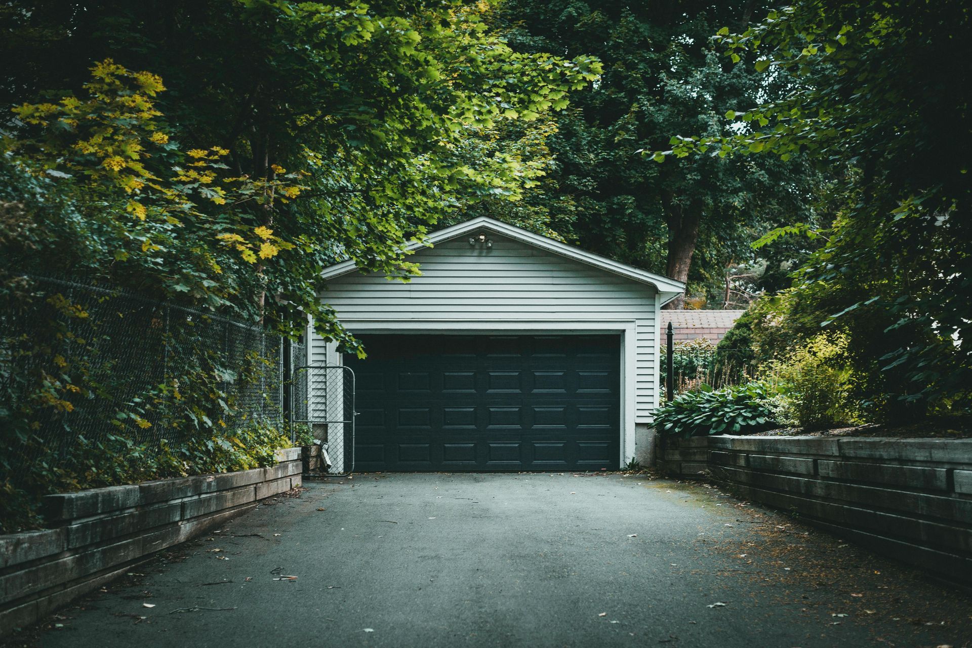 A garage with a black door is surrounded by trees.