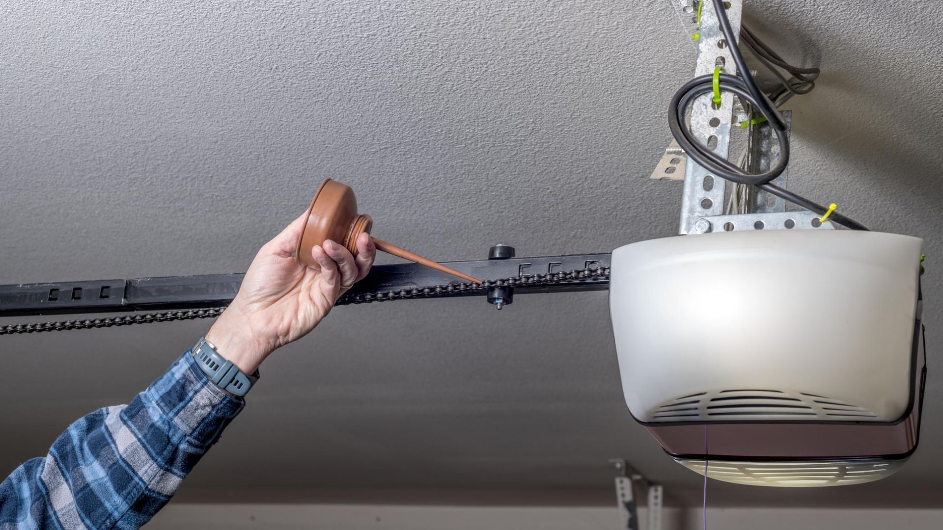 A person holds an oil can to lubricate the chain on a garage door opener motor rail.