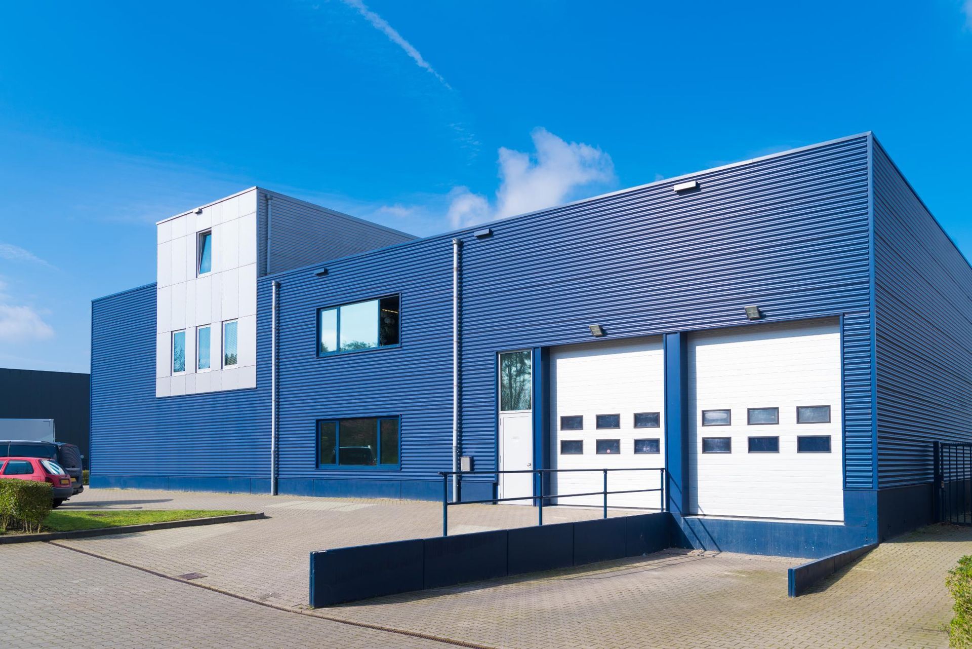 A modern, two-story commercial building with blue corrugated metal siding, white roll-up garage doors, and a paved lot.