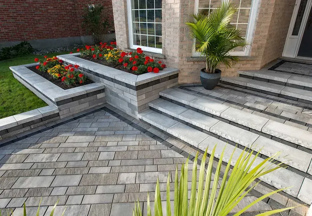 Fair Haven NJ Paver landscaping company. Modern brick house patio with raised flower beds, gray paver walkway, and a potted palm by the steps