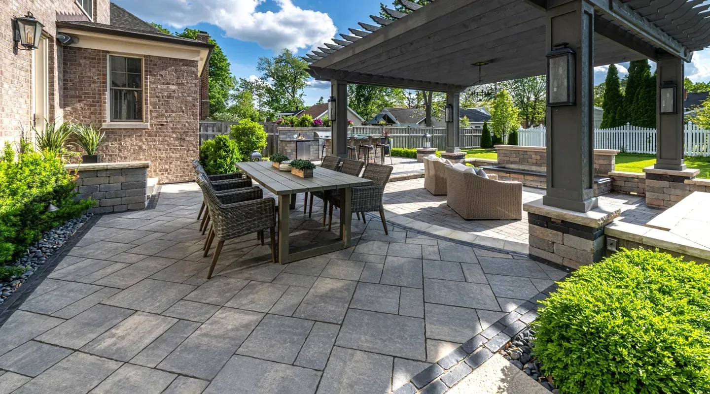 Patio with stone pavers in Holmdel , outdoor dining table, covered seating area, and manicured shrubs beside a brick building