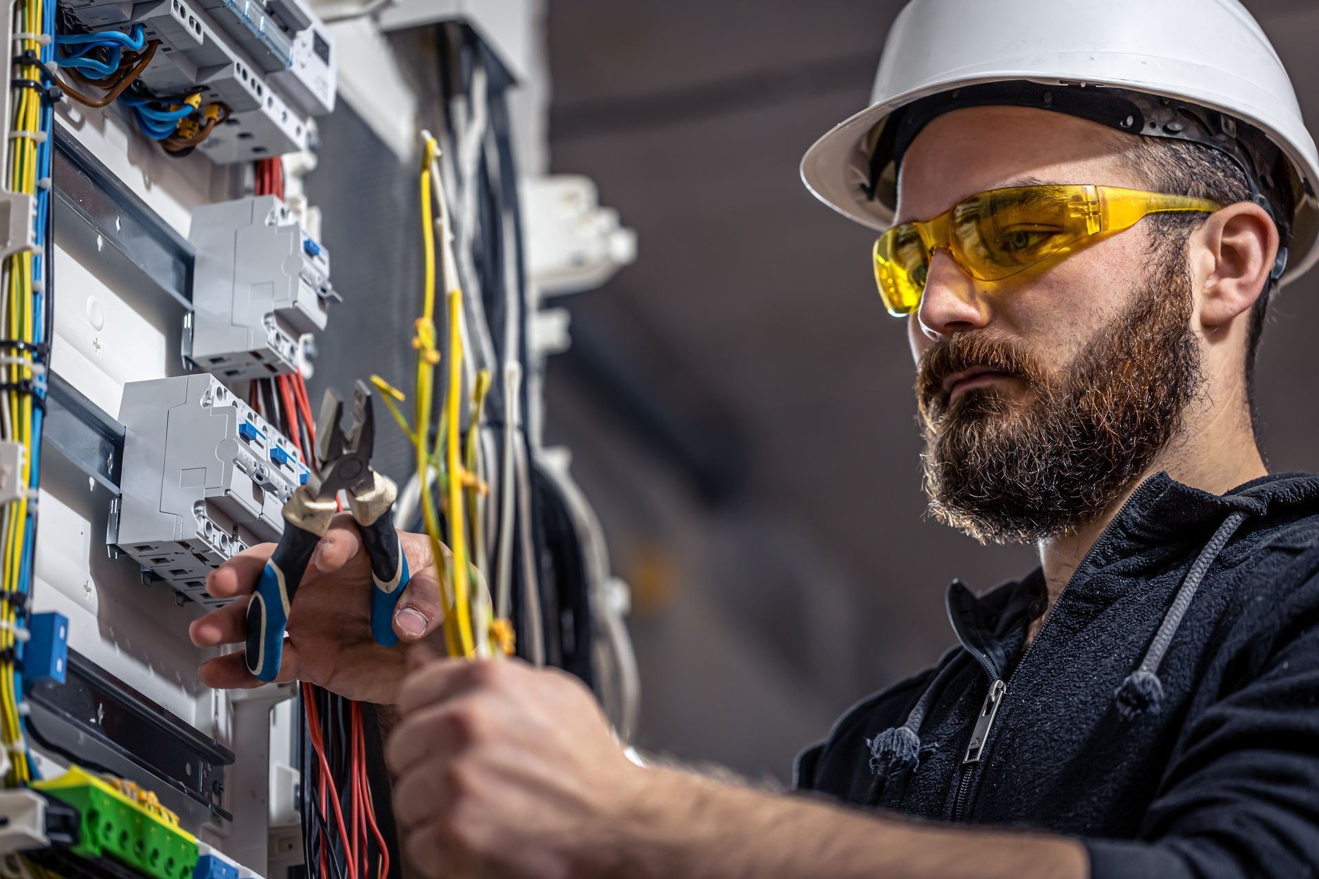 A man wearing a hard hat and safety glasses is working on an electrical box.