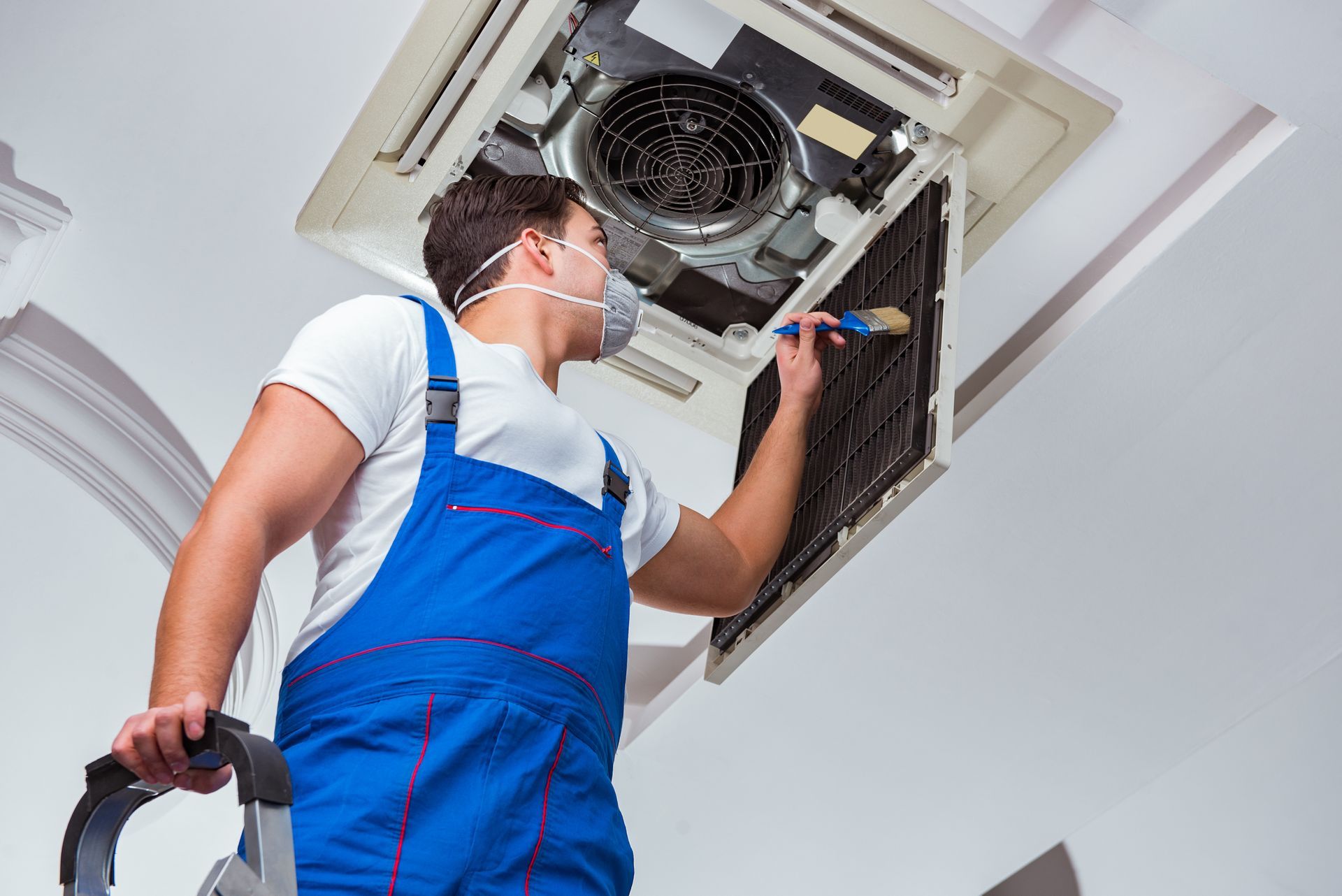 A man wearing a mask is cleaning a ceiling fan.