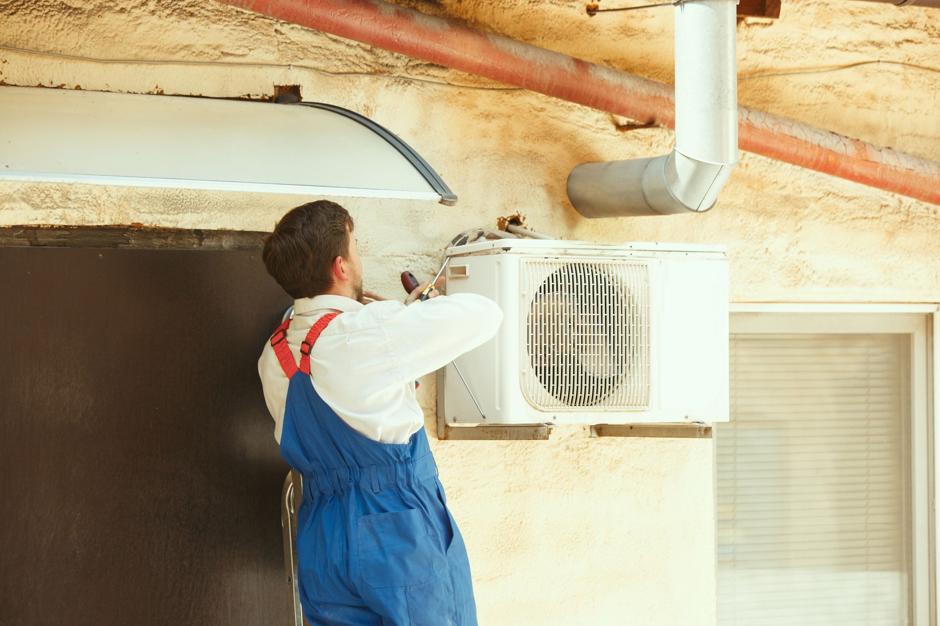 A man is installing an air conditioner on the side of a building.