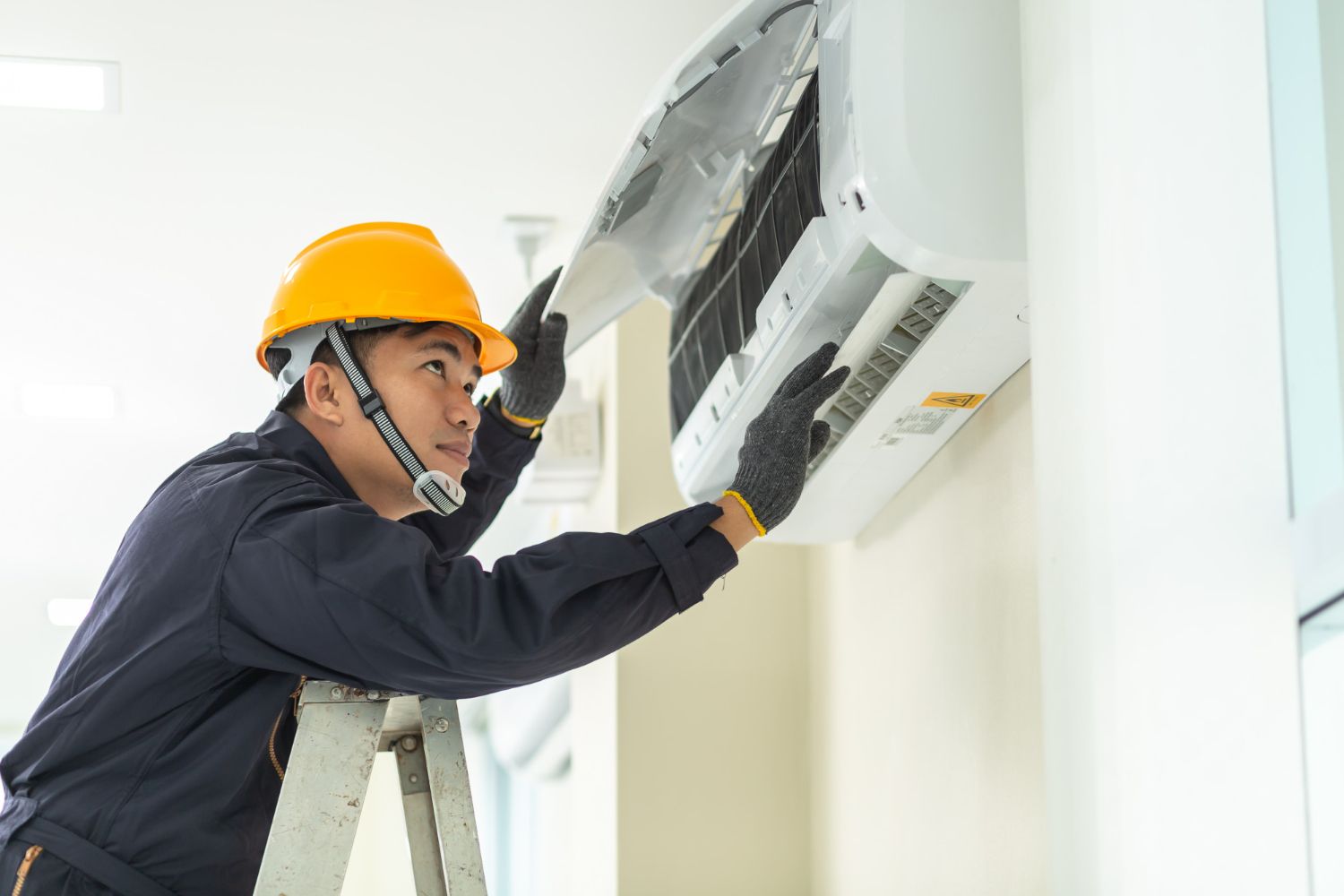 A man is standing on a ladder fixing an air conditioner.
