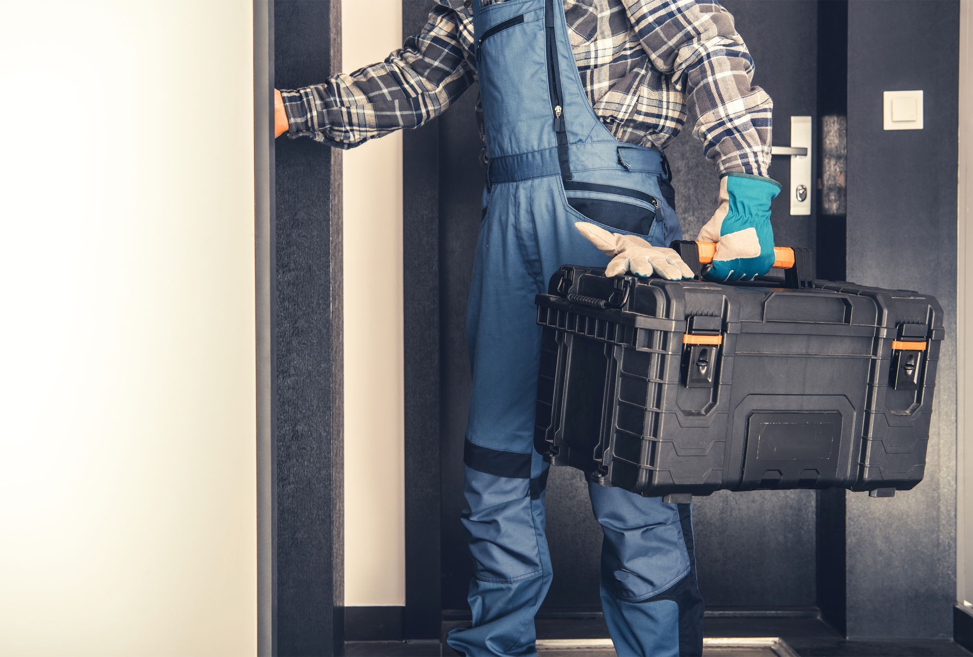 A man is holding a toolbox and a drill while standing in front of a door.
