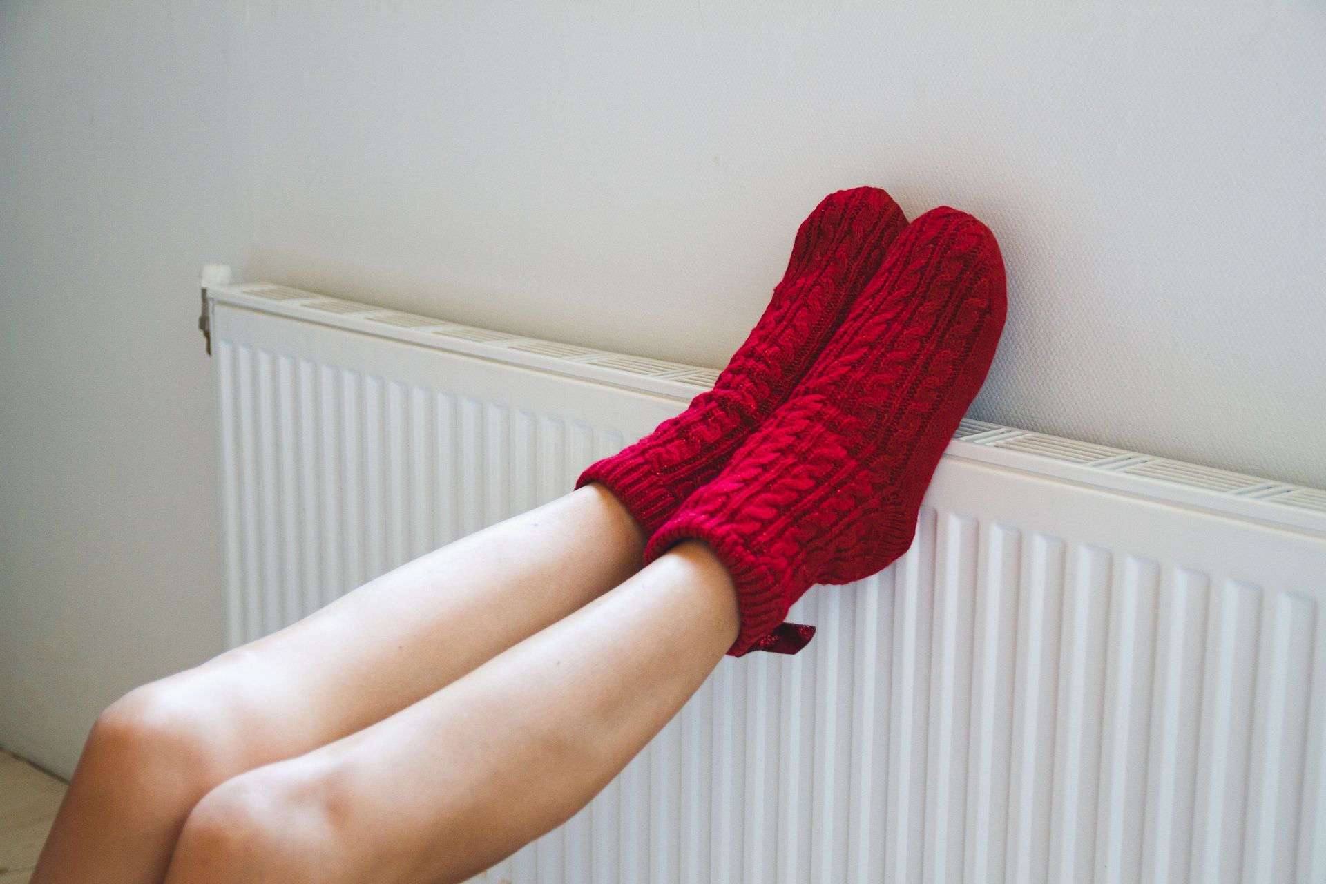 A woman wearing red socks is leaning against a radiator.