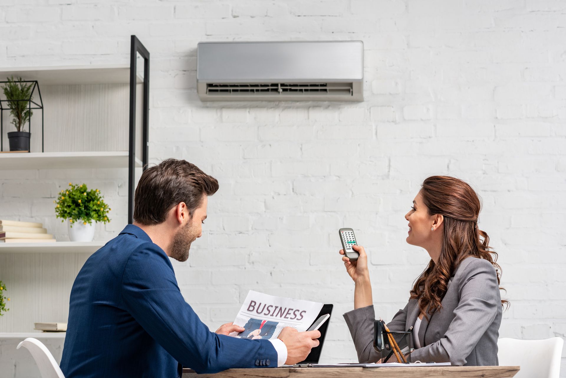 A man and a woman are sitting at a table under an air conditioner.