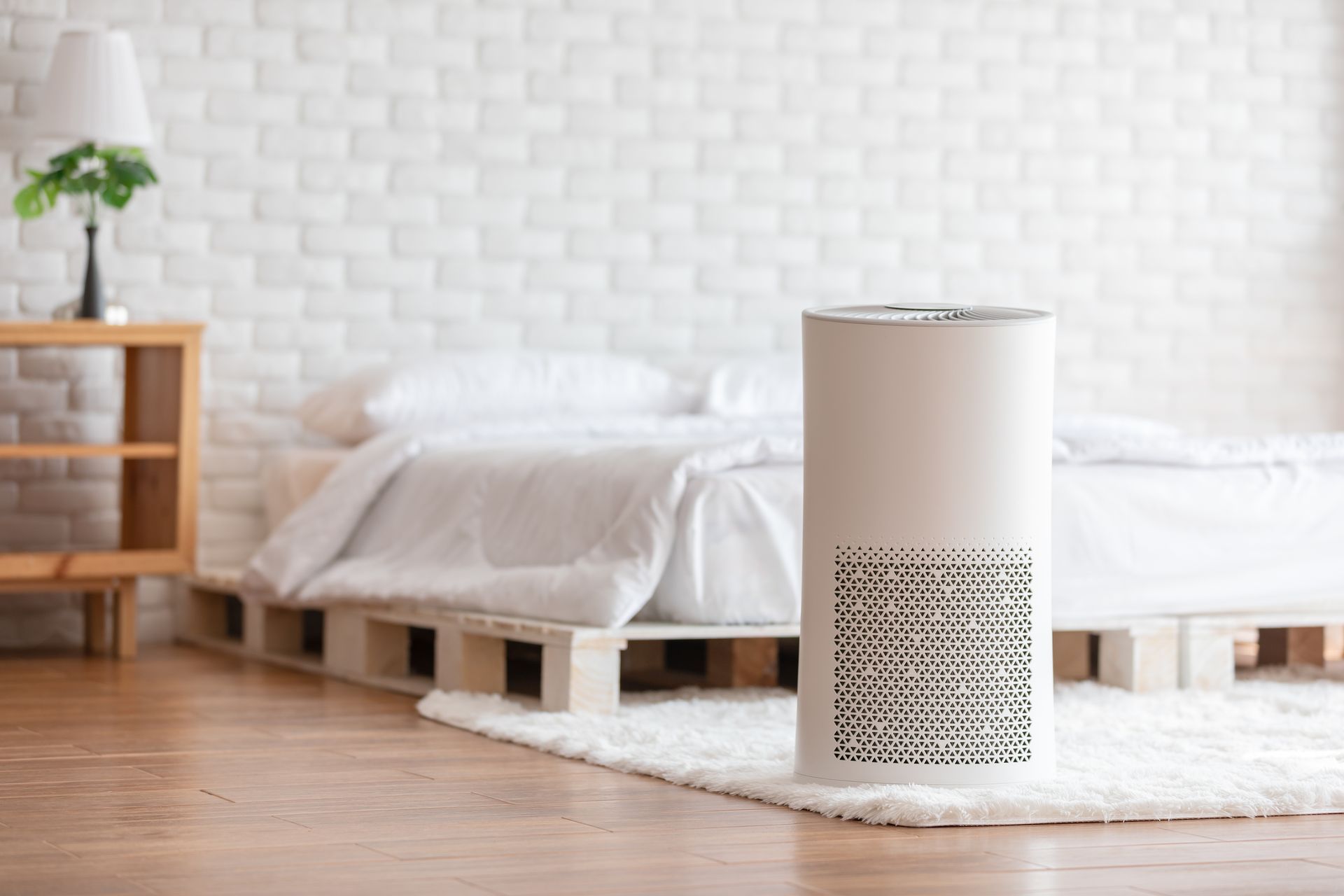 A bedroom with a bed and a air purifier on the floor.