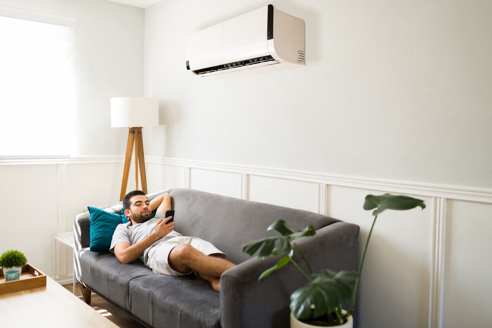 A man is laying on a couch in a living room using a cell phone.
