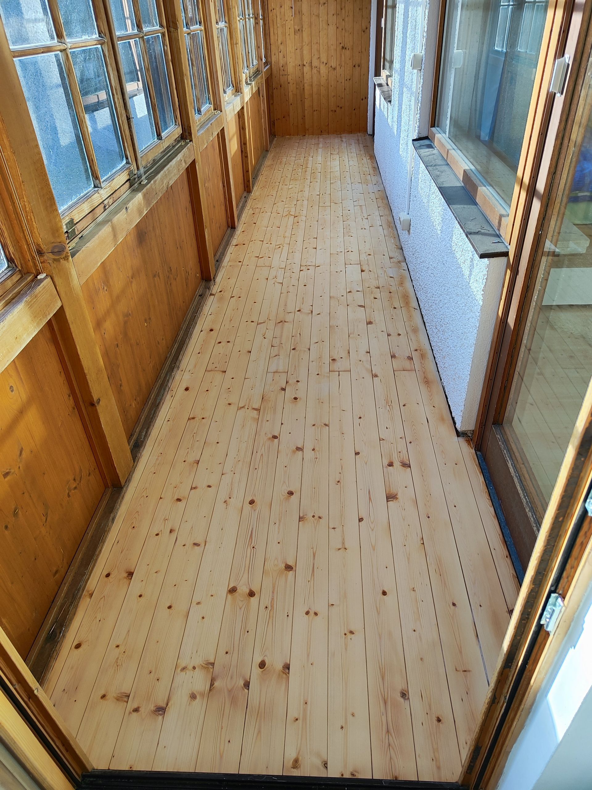 Ein langer Holzflur mit vielen Fenstern und einem Holzboden.