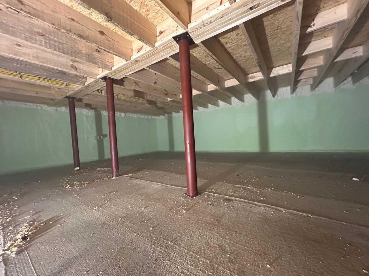 Basement with wood joists and support columns. Light green walls, concrete floor.