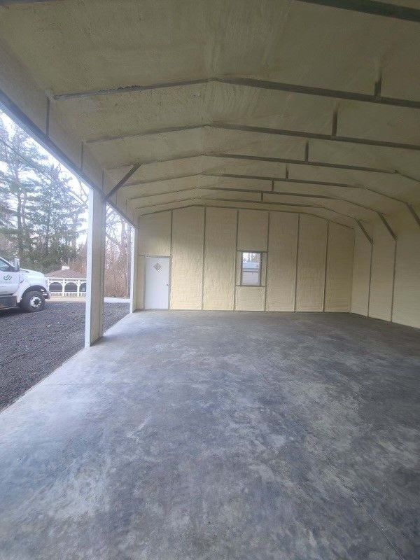 Interior of a building with light-colored spray foam insulation on walls and ceiling, concrete floor, and a door.