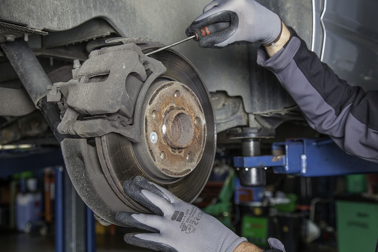 Mechanic holding a brake rotor and caliper while inspecting a car wheel assembly on a lift