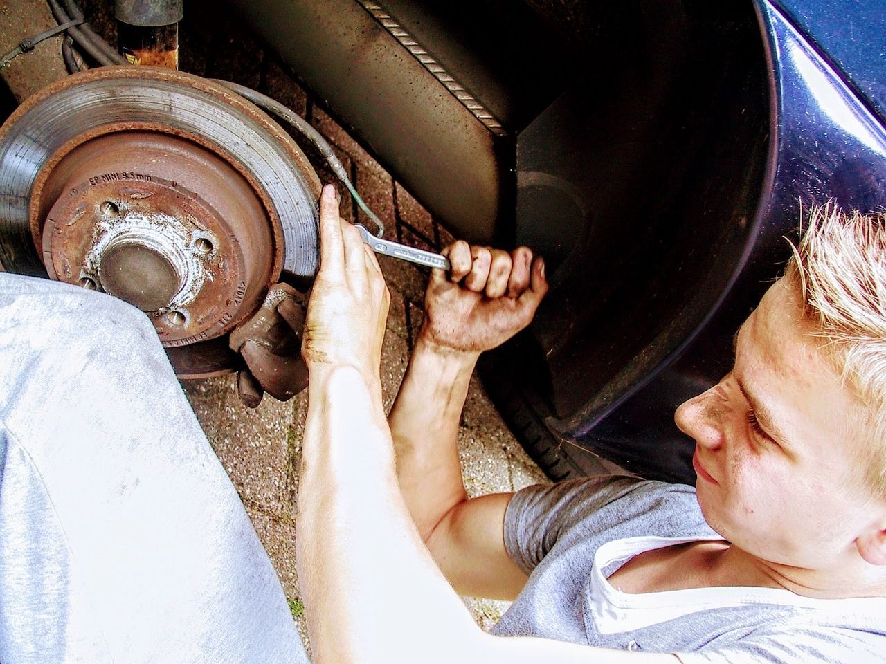 Person working under a car, tightening a wheel nut with a wrench.