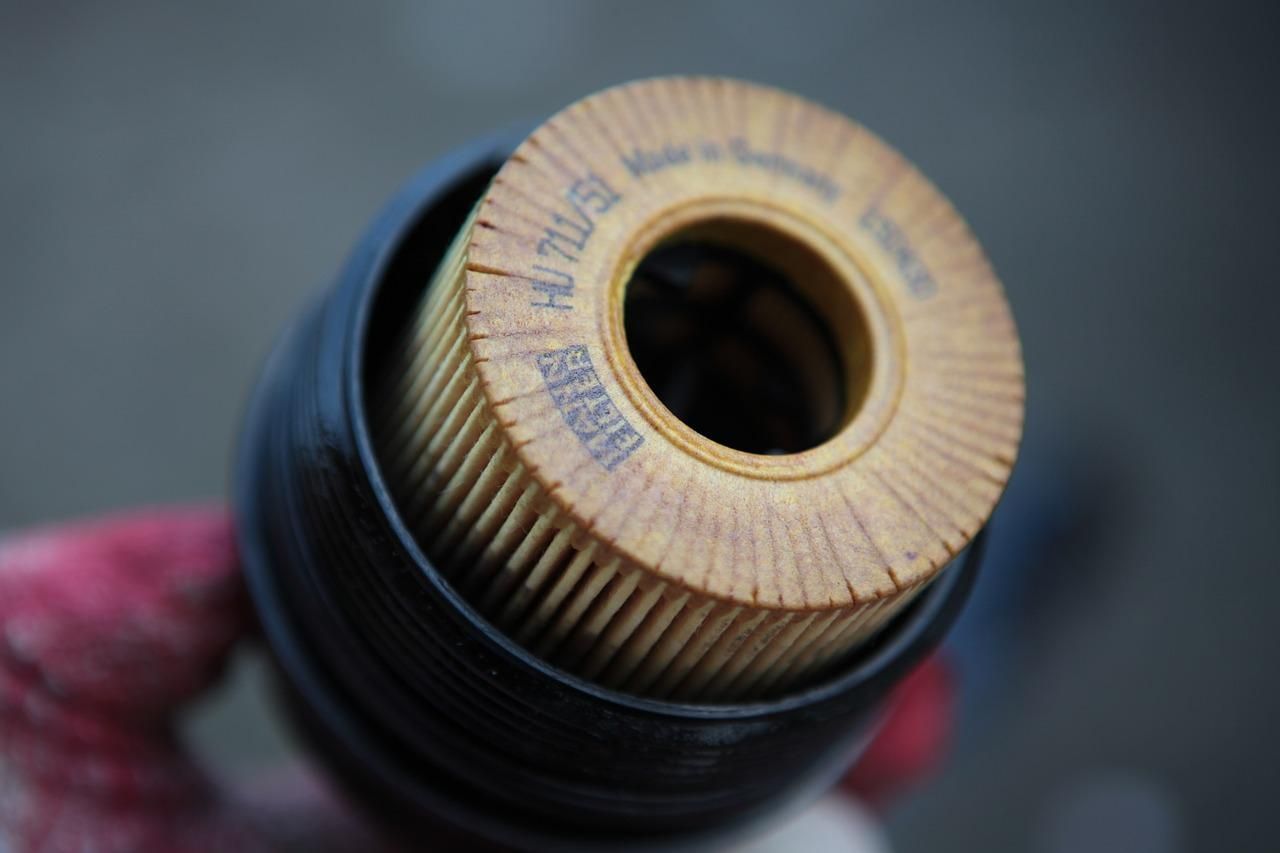 Close-up of a beige pleated air filter cartridge in a black housing, held by a gloved hand