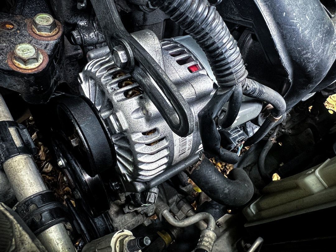 Close-up of a car engine with a silver alternator and black hoses covered in grime.