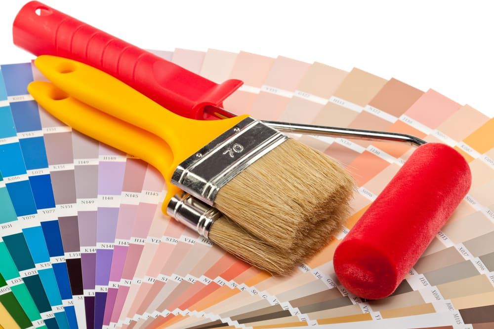 Three Paint Brushes And A Paint Roller Are Sitting On Top Of A Color Palette — Ballina Painting Service In Ballina, NSW