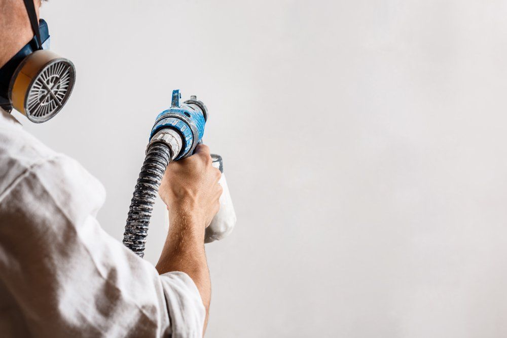 A Man Wearing A Gas Mask Is Spraying Paint On A Wall — Ballina Painting Service In Ballina, NSW