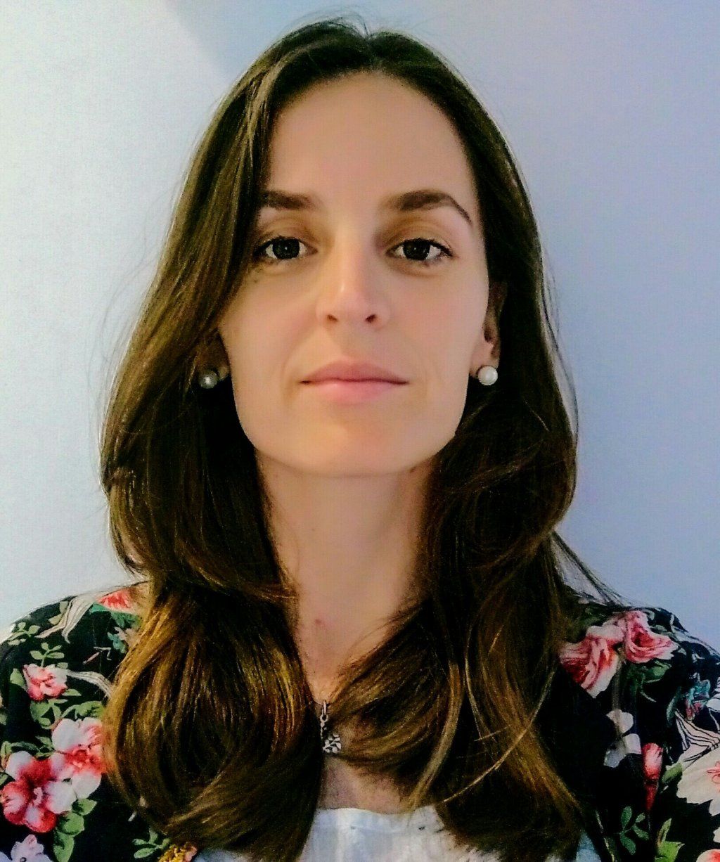 Mujer con cabello castaño y chaqueta floral, mirando a la cámara.