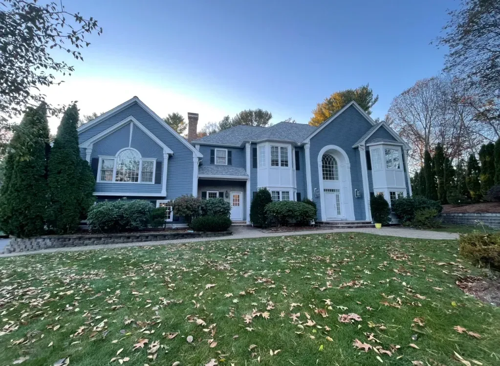Blue and white two-story house with a large lawn and autumn leaves. The sky is clear.
