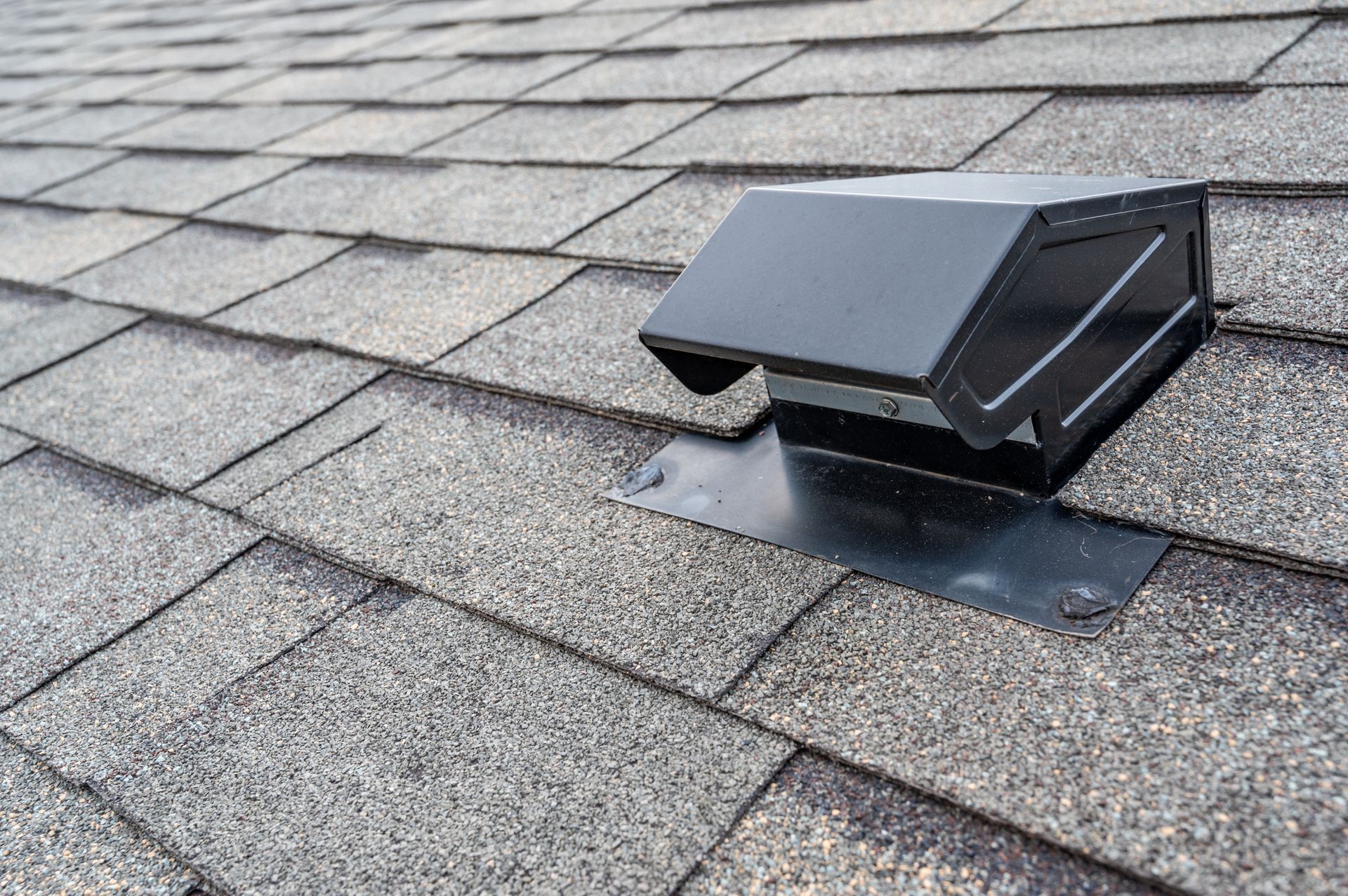 Black roof vent installed on gray asphalt shingles.