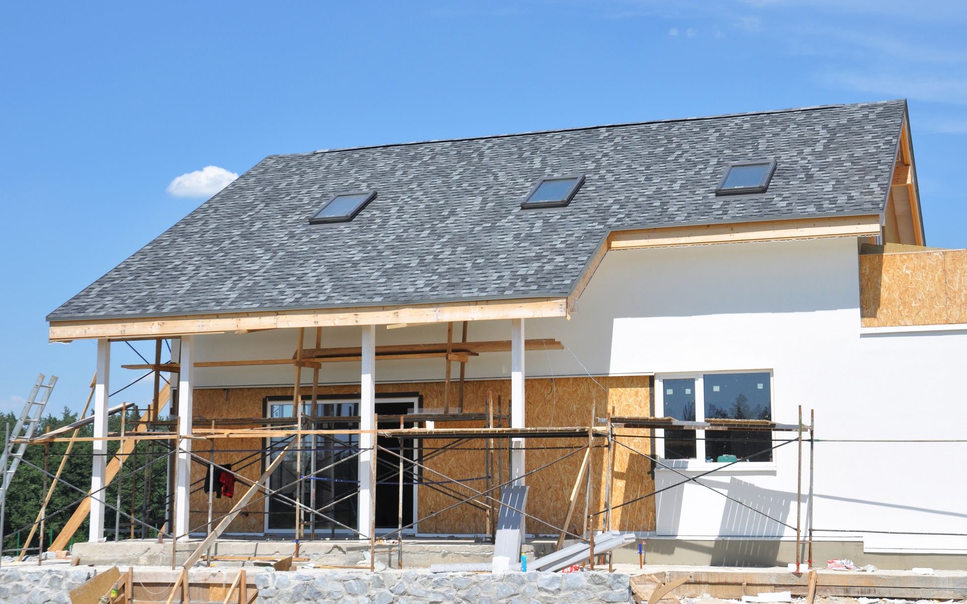 Construction of a house with gray shingled roof, skylights, and scaffolding.
