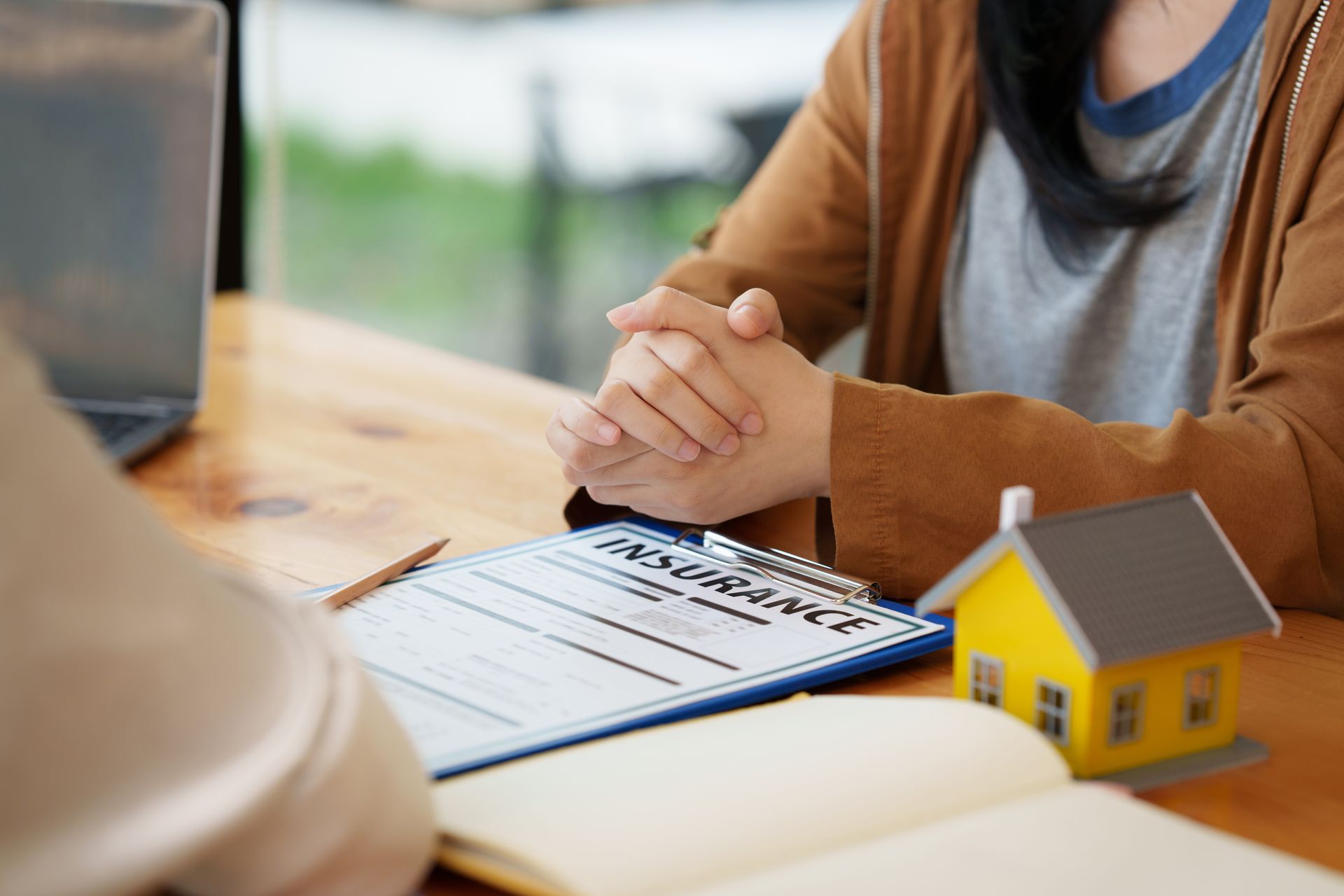 Two people reviewing documents at a desk with a small yellow house model and laptop nearby