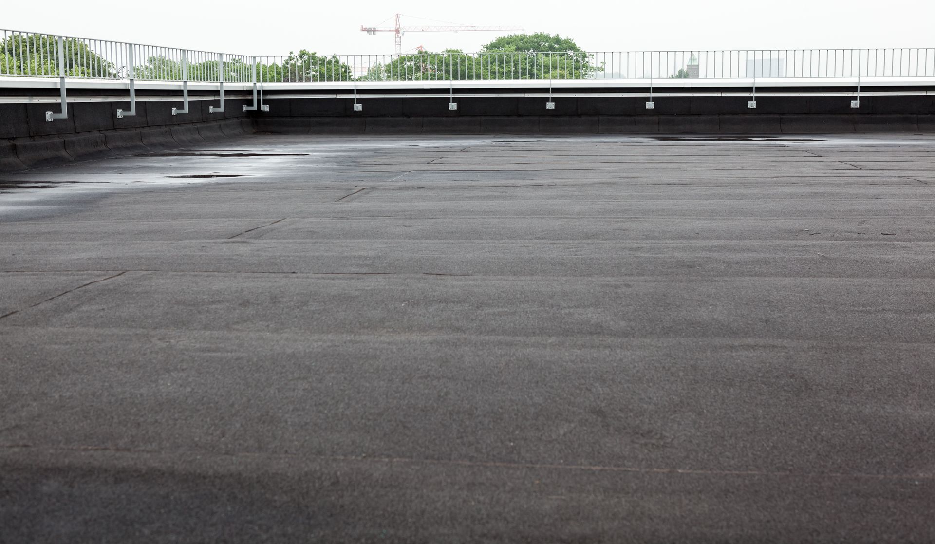 Empty rooftop parking lot with dark asphalt and a low white railing under an overcast sky