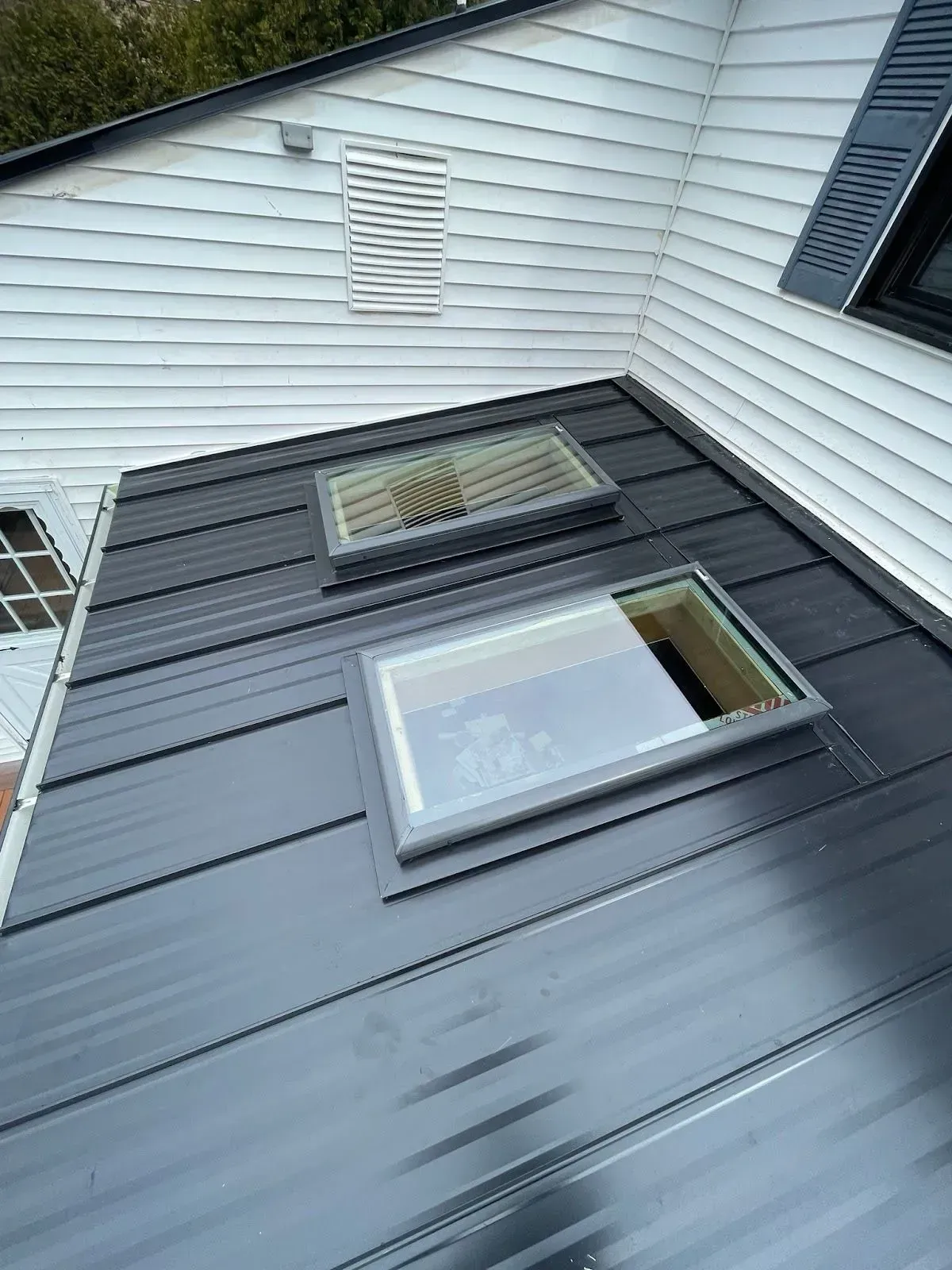 Gray metal roof with two skylights against white siding and a dormer window