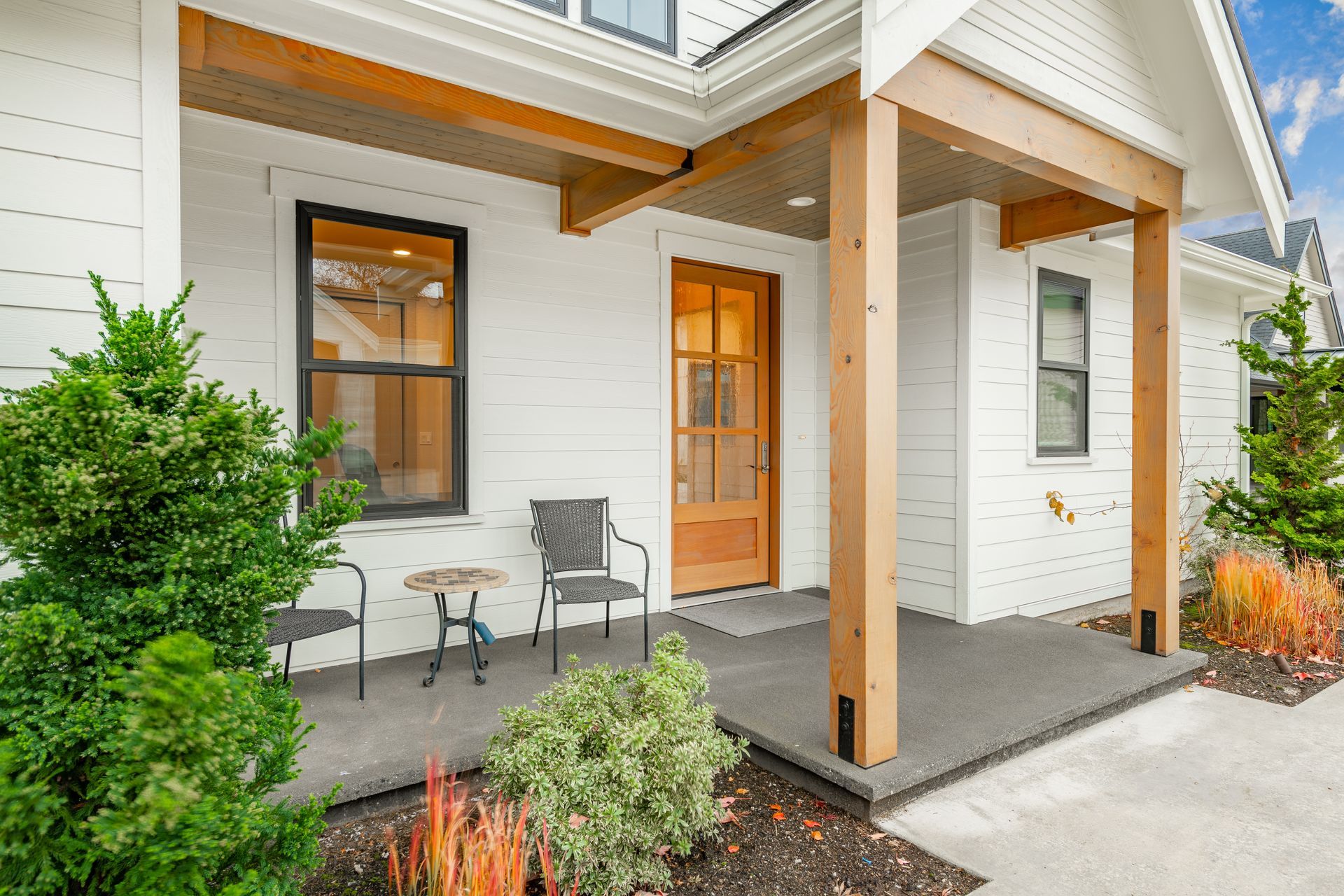 Covered front porch with wooden columns, gray siding, orange door, and two chairs beside a small table.