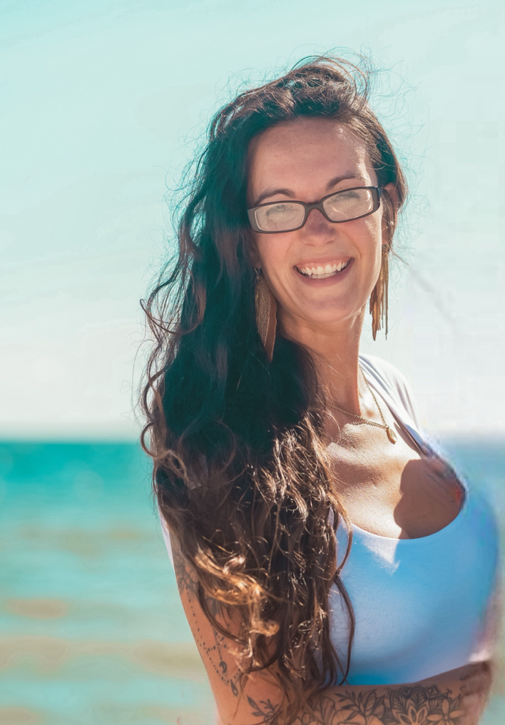 A woman wearing glasses and a blue off the shoulder top is standing on a beach.