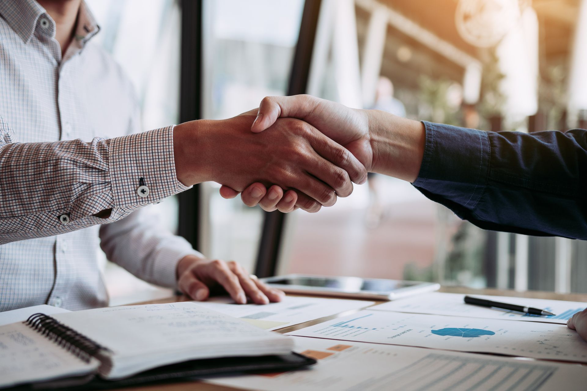 Two men shaking hands over a desk with papers, office setting, agreement.