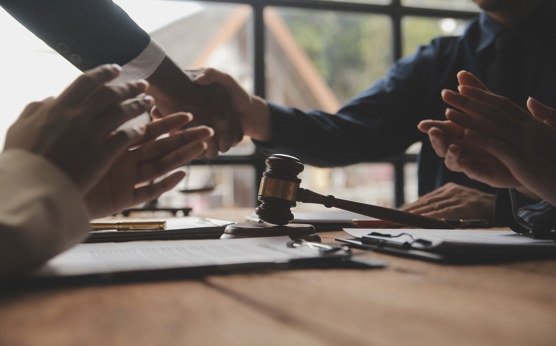 People shaking hands at a table, gavel in front, others clapping, possibly a legal or business agreement.