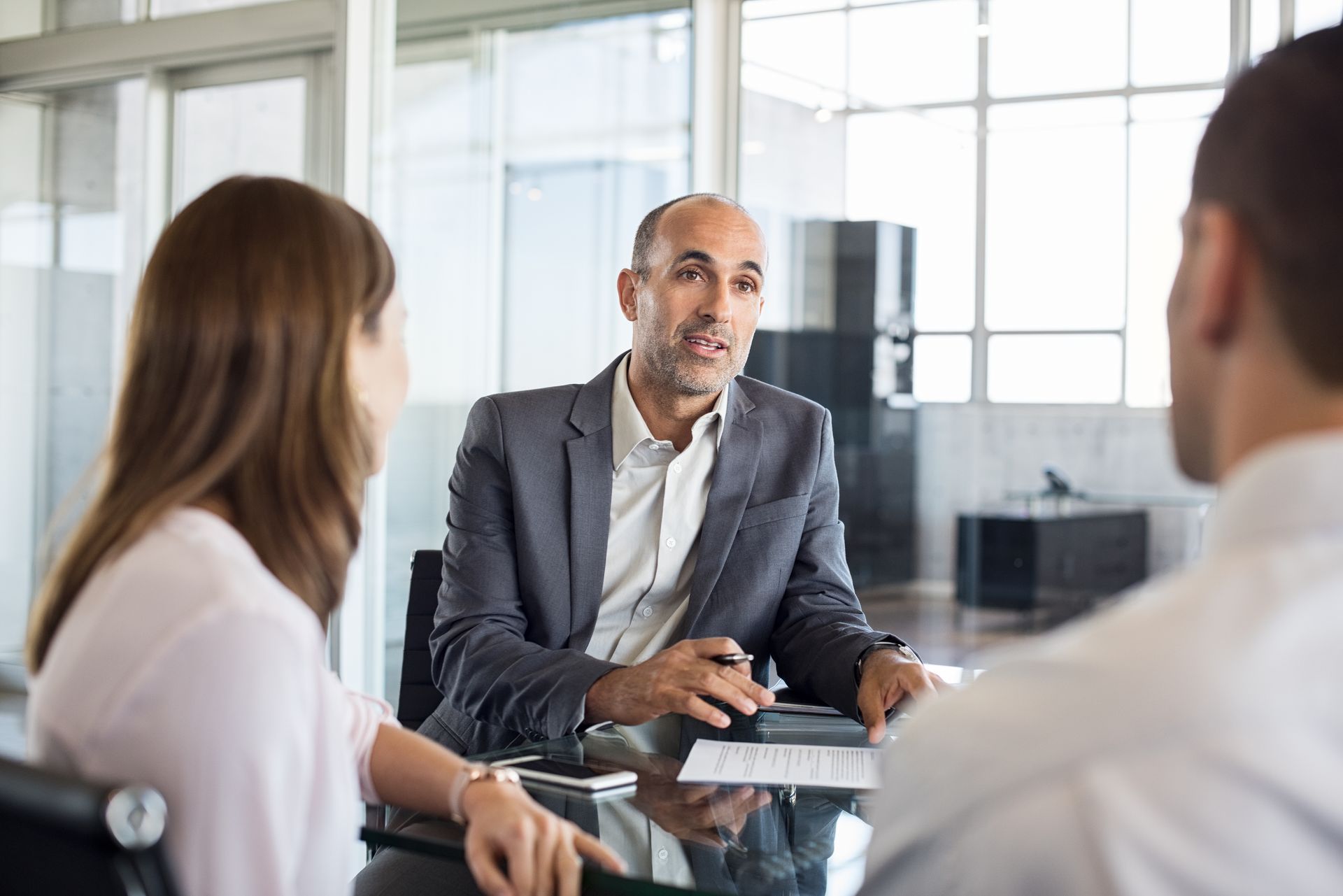A financial advisor in a suit speaks with a couple at a table in an office.