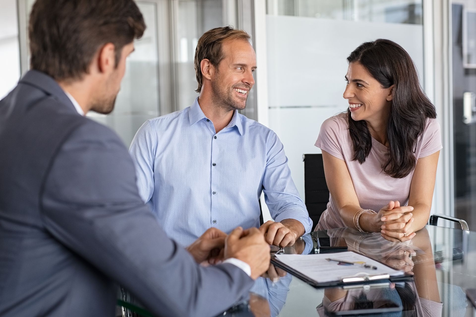 A financial advisor sits with a smiling couple at a desk in an office.