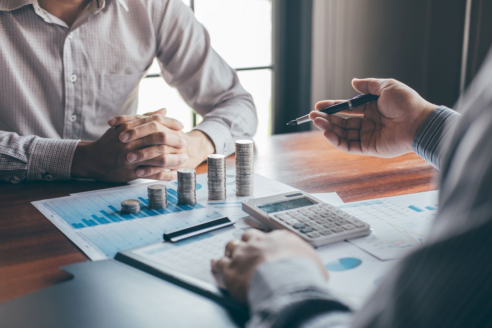 Two people reviewing financial documents with coins, a calculator, and a pen on a desk.