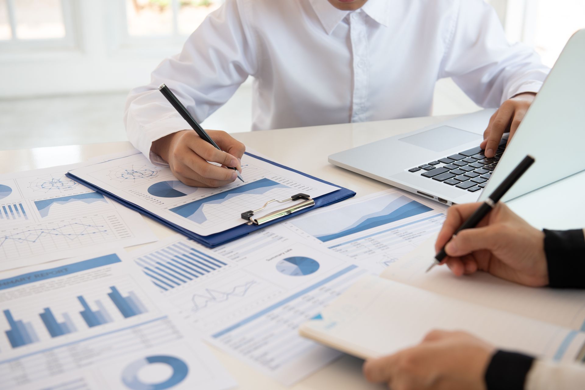 Two people reviewing financial charts and data on a table with a laptop.