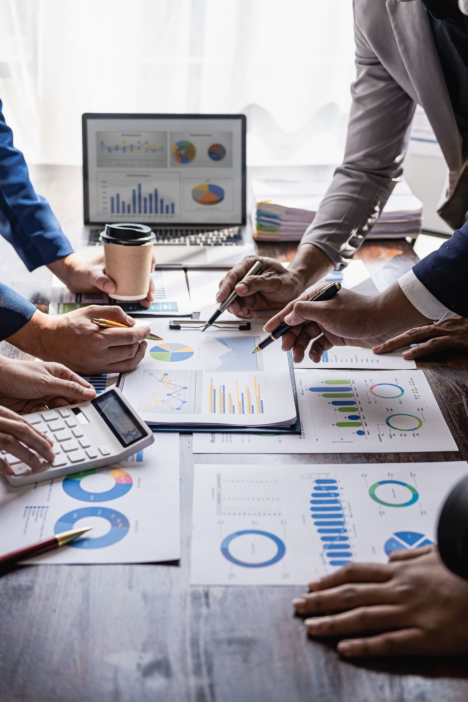 People analyzing charts and data on a table, with laptop and calculator.