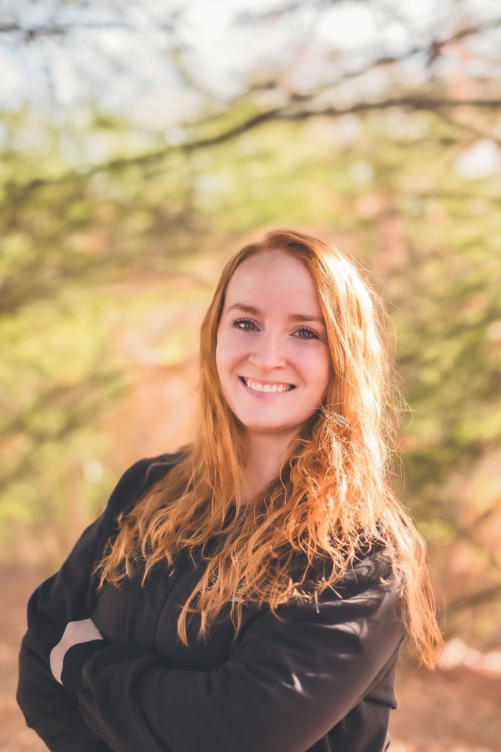 a woman with red hair is standing with her arms crossed and smiling .