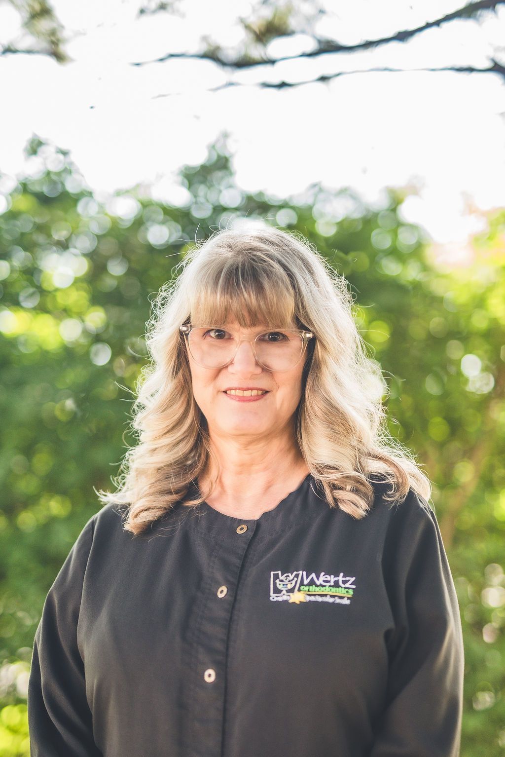 a woman in a black jacket is standing in front of trees .