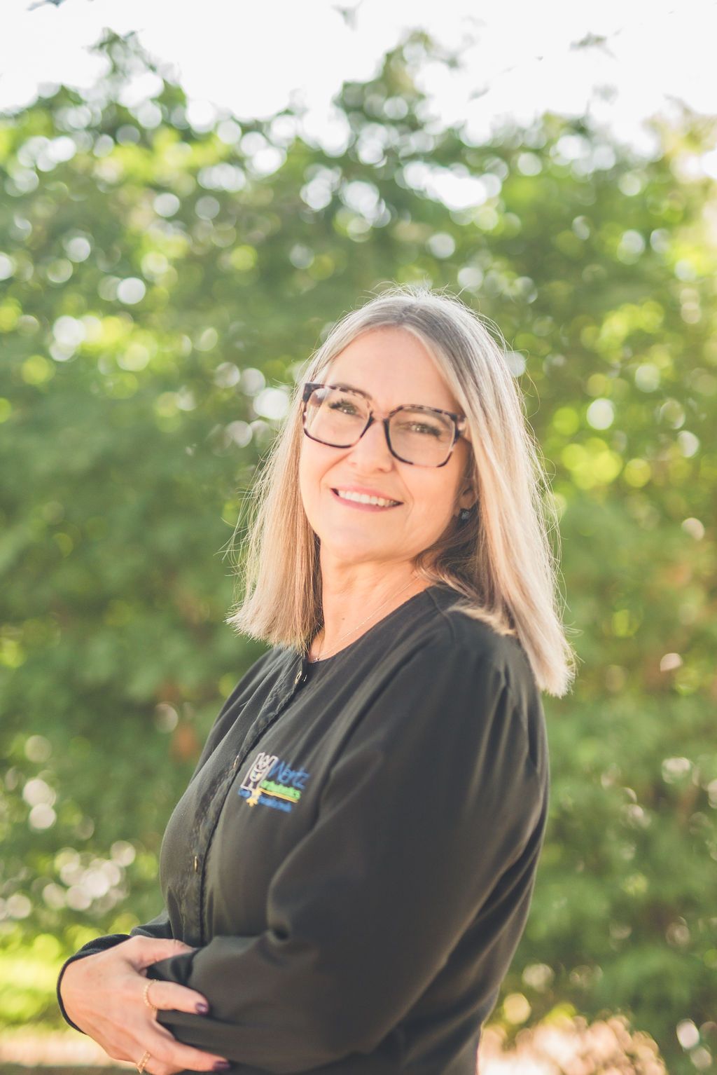 a woman wearing glasses and a black jacket is standing in front of a tree .