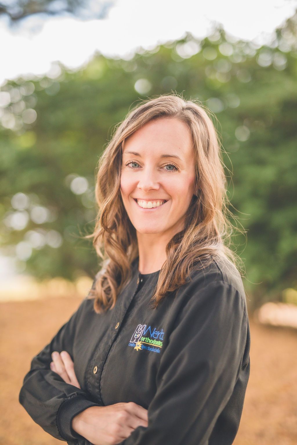 a woman in a black jacket is standing with her arms crossed and smiling .