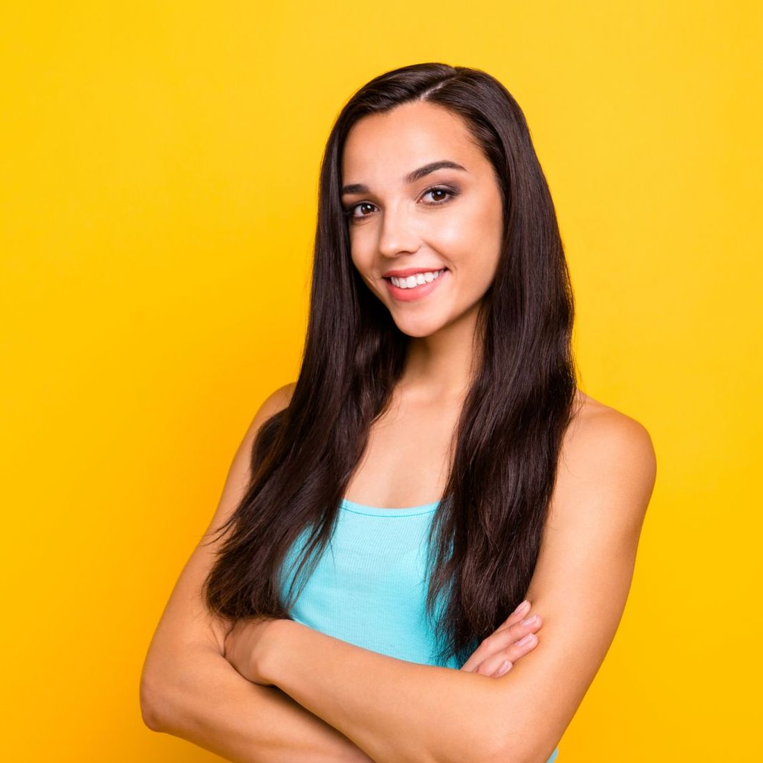 A woman with long hair is standing with her arms crossed and smiling.