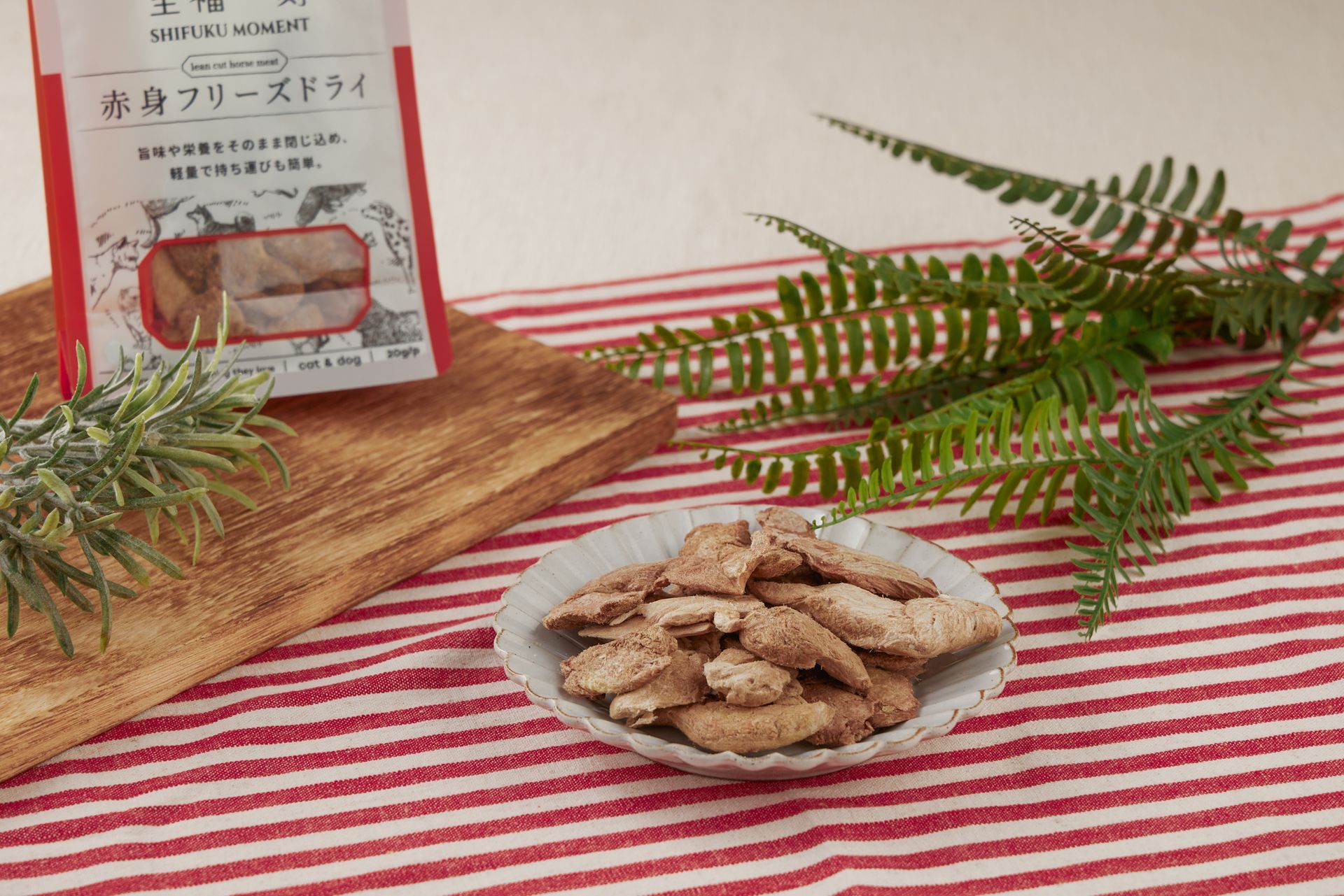 冷凍乾燥食品放在碗裡，旁邊有一個包裝袋，放在鋪著紅白條紋桌巾的木板上，還有綠植點綴。