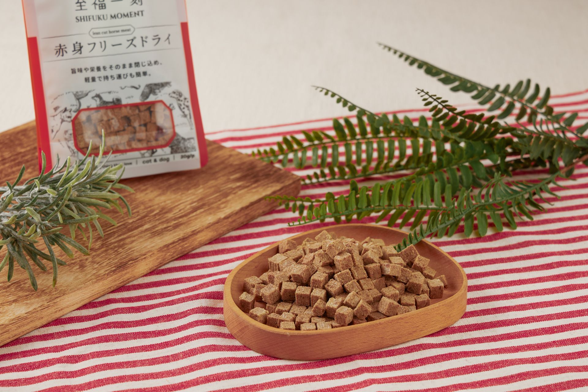 冷凍乾燥食品放在碗裡，旁邊有一個包裝袋，放在鋪著紅白條紋桌巾的木板上，還有綠植點綴。