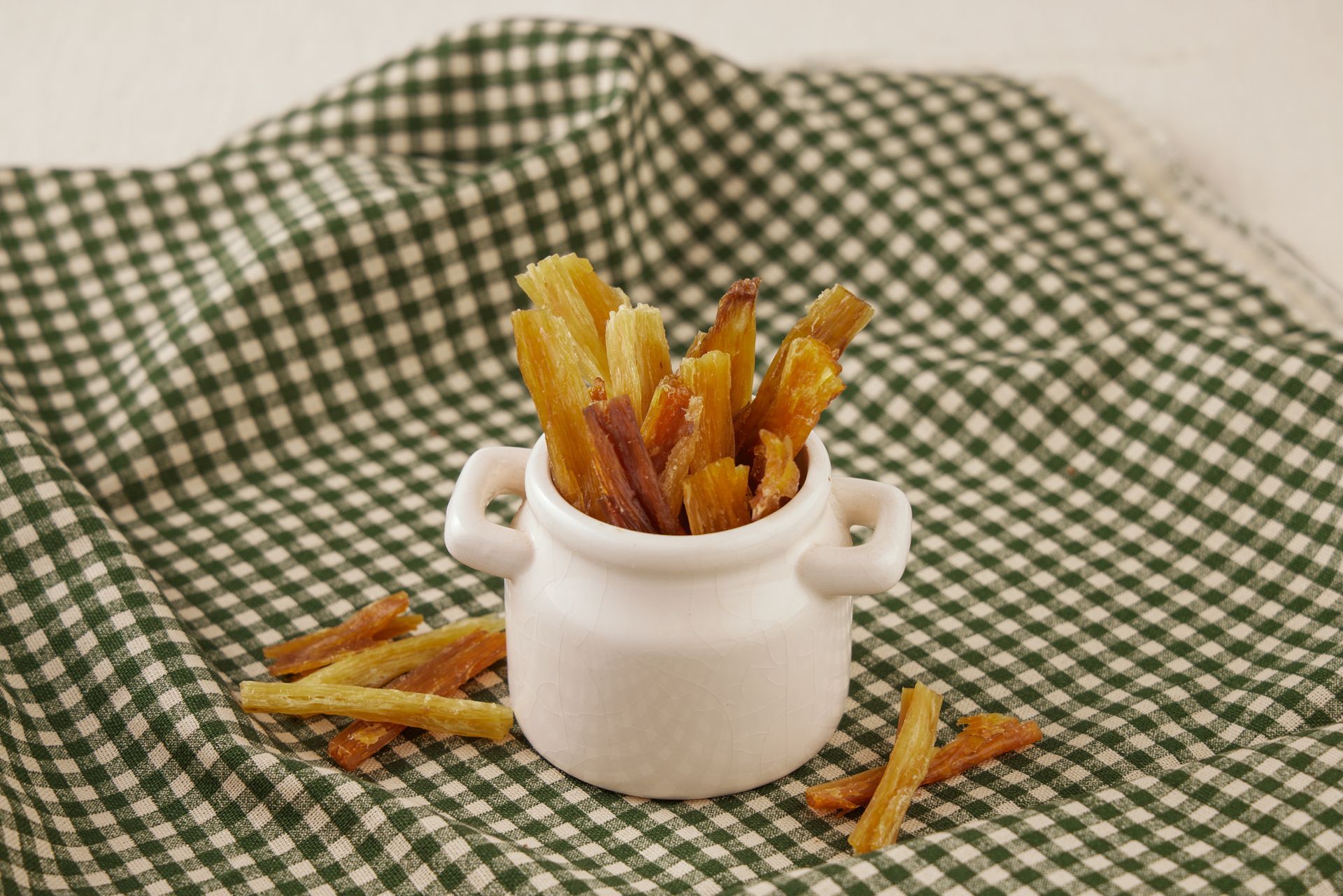 盛在小白罐裡的紅薯條，放在綠白相間的格子佈上。