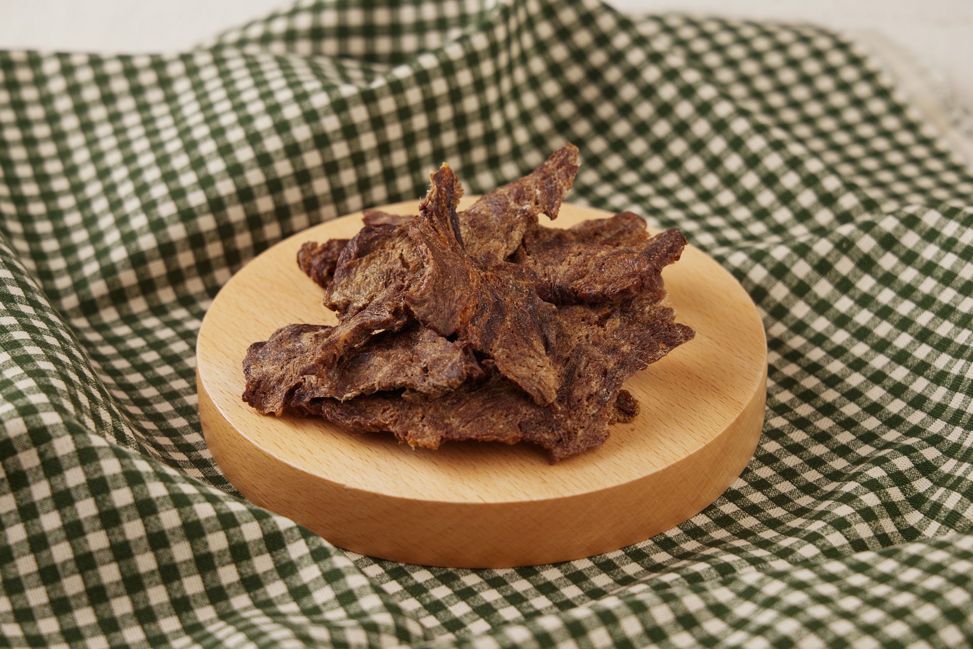 牛肉乾放在木質砧板上，砧板上鋪著綠白相間的格子佈。